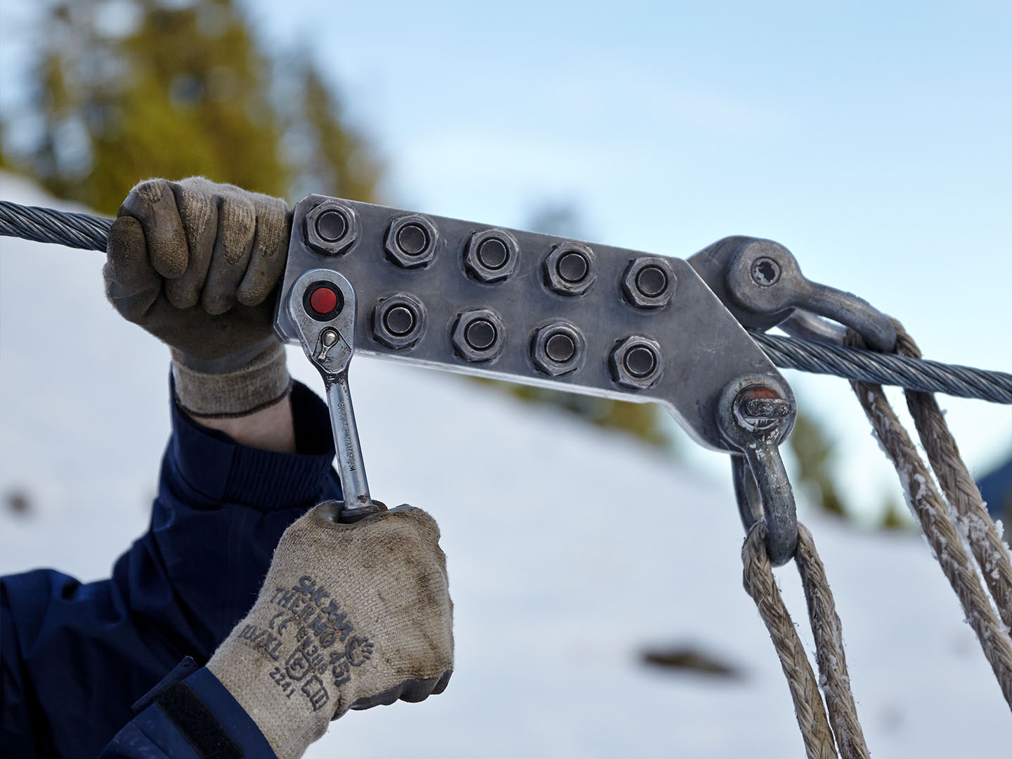 Two hands in gloves of a worker on a snowy mountain adjusting a cable clamp 